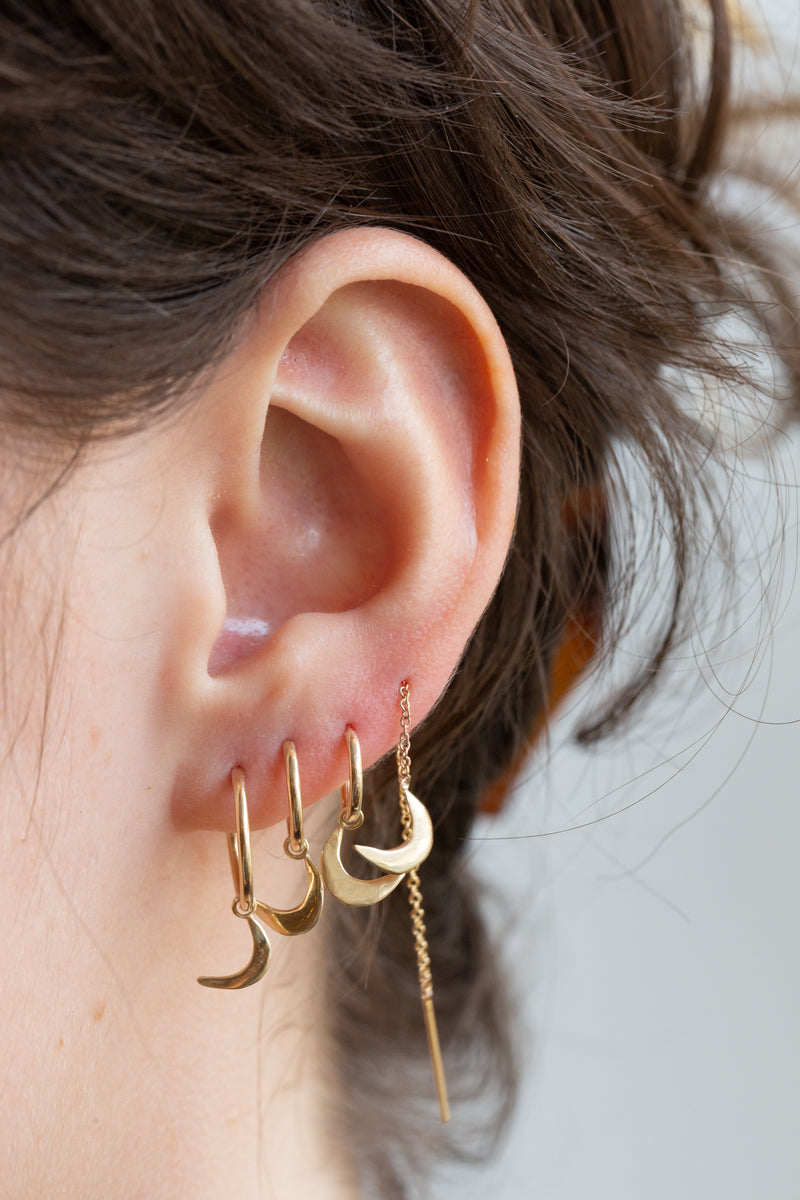 Person wearing several Moon+Arrow's 10kt yellow gold crescent moon on gold fill endless hoops