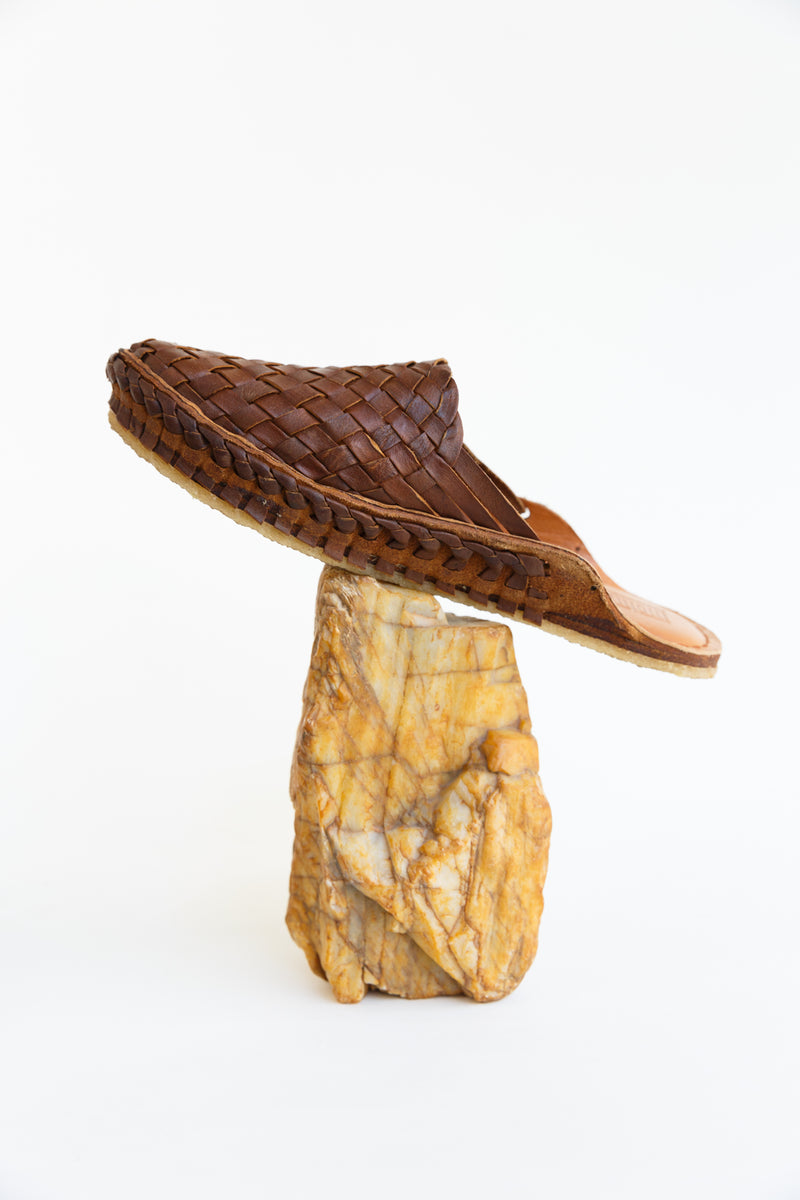 Person wearing a pair of Mohinders Woven Slide shoe in walnut laying on top of a rock