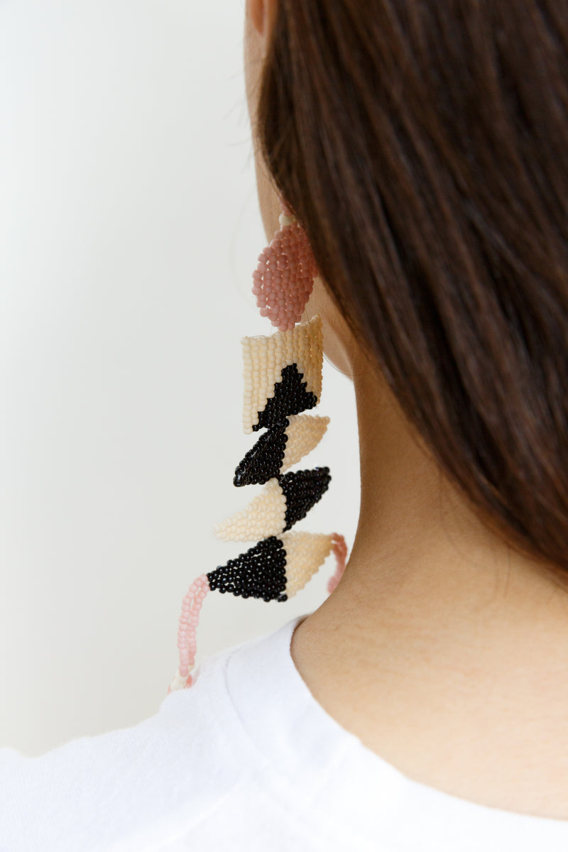 A brown-haired woman wearing unique beaded earrings created by Create Share Repeat for Moon+Arrow. The earrings feature intricate beadwork and showcase the brand's commitment to one-of-a-kind, distinctive designs