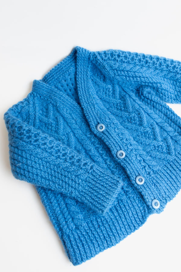 1960s handknit blue chunky cardigan with buttons from Gus & Way, featuring a classic cable knit design. Ideal for adding vintage charm and warmth to children’s fashion.