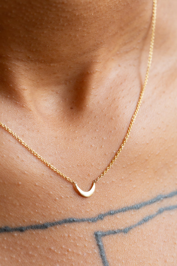 Person wearing Moon+Arrow's fine jewelry crescent moon necklace in 10kt yellow gold on a 10kt yellow gold chain