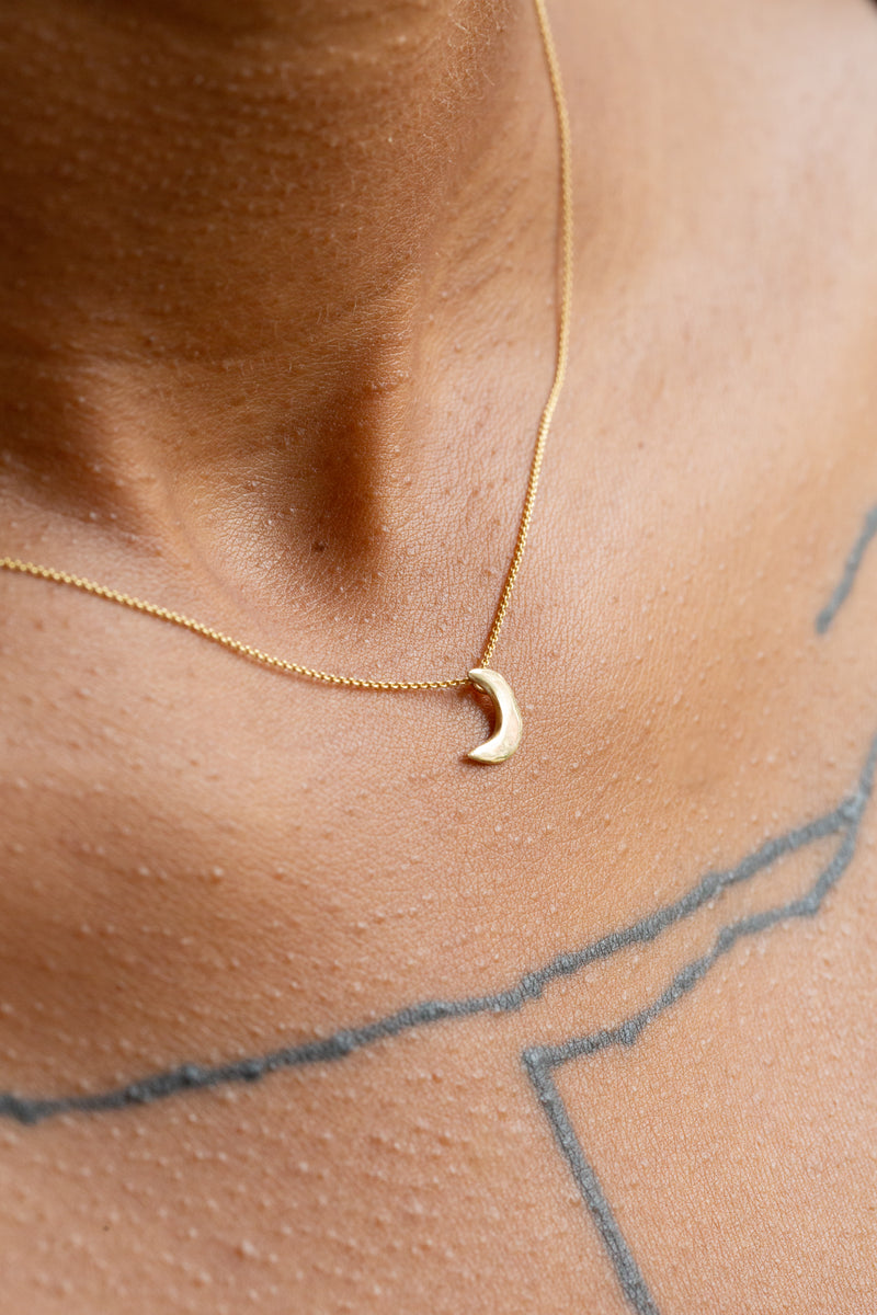 Person wearing Moon+Arrow's fine jewelry mini luna 10kt yellow gold crescent moon necklace