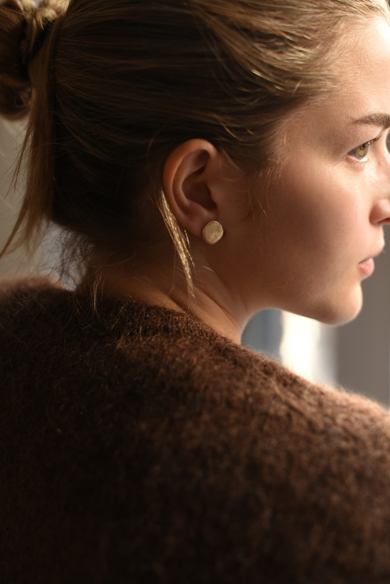 Person wearing beautifully textured brass stud earrings, handcrafted in NYC by 8.6.4.