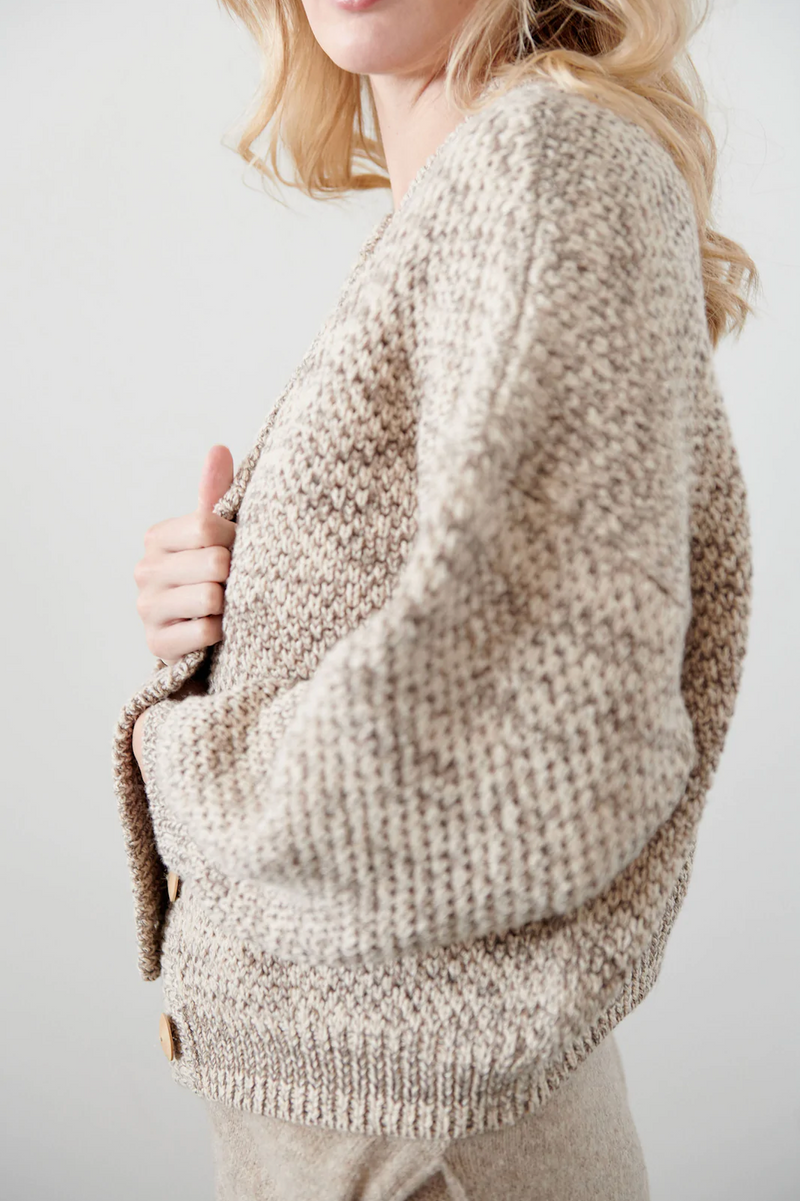 A model is wearing a cropped wide cardigan featuring unvarnished wood buttons and a high, rounded collar made of wool/alpaca blend chain yarn