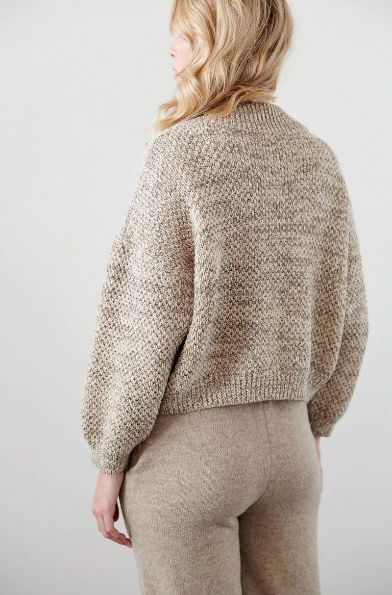 A model wearing a cropped wide cardigan featuring unvarnished wood buttons and a high, rounded collar made of wool/alpaca blend chain yarn