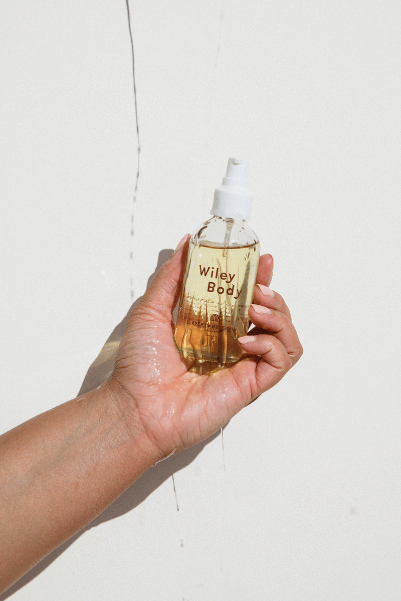 A person holding a bottle of Wiley Body Everywhere Oil, crafted from a skin-loving botanical blend of lightweight cold-pressed oils