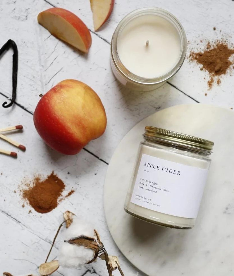 A Brooklyn Candle Studio jar in Apple Cider scent on a table with apples