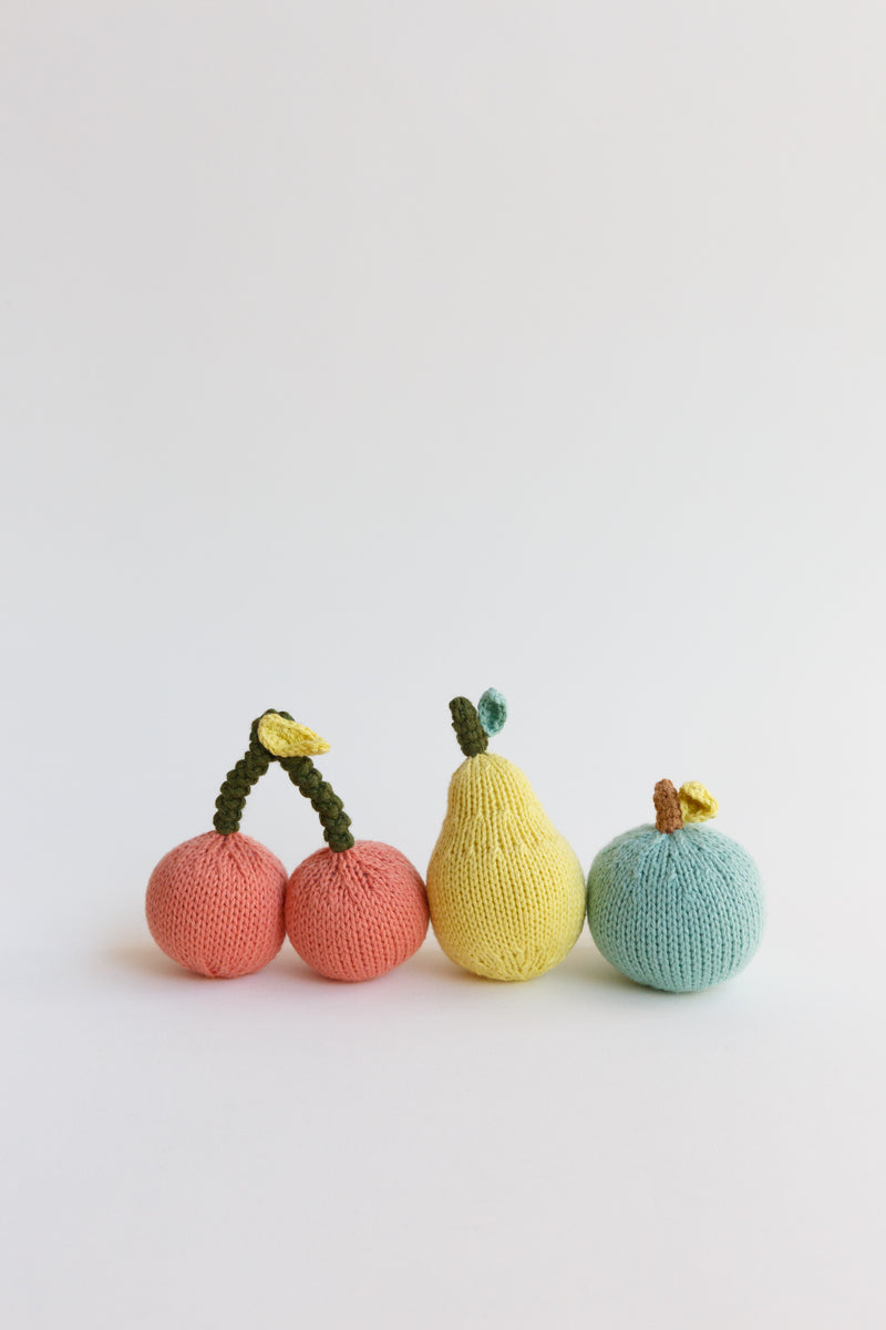 A collection of blabla fruit rattles, apple, pear, and cherries, made of 100% cotton knit and handmade in Peru