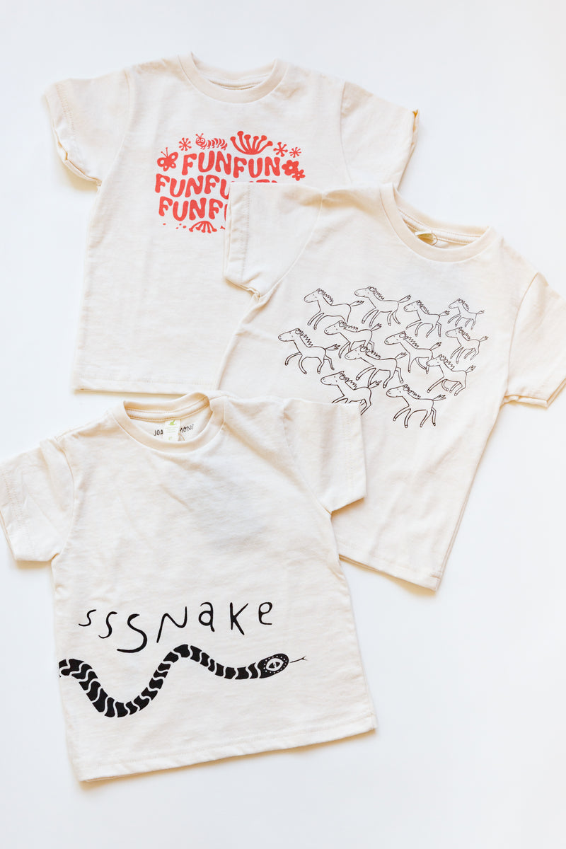 A baby Joan Ramone snake t-shirt made of 100% organic cotton with a slithering snake hand-printed on front and back, laying flat on a table with other shirts