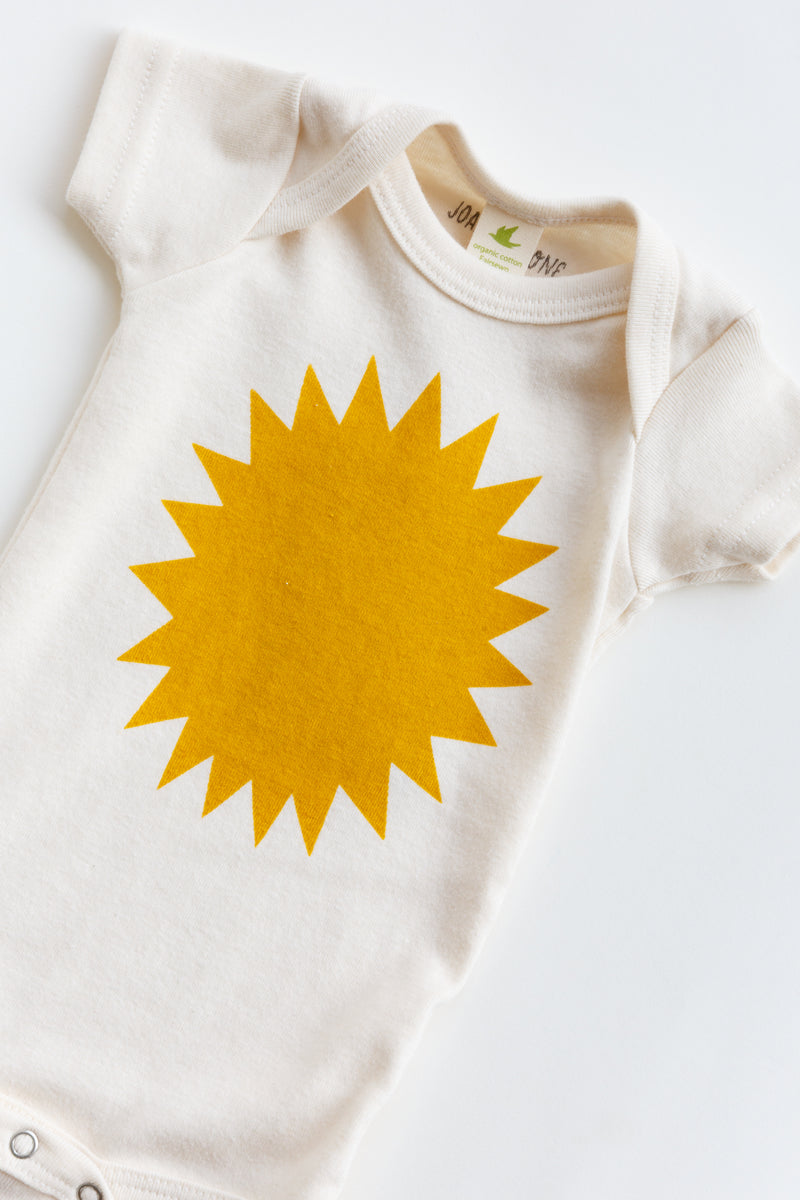 A Joan Ramone baby sunshine onesie printed on 100% organic cotton with non-toxic, water-based ink, laying flat on a table
