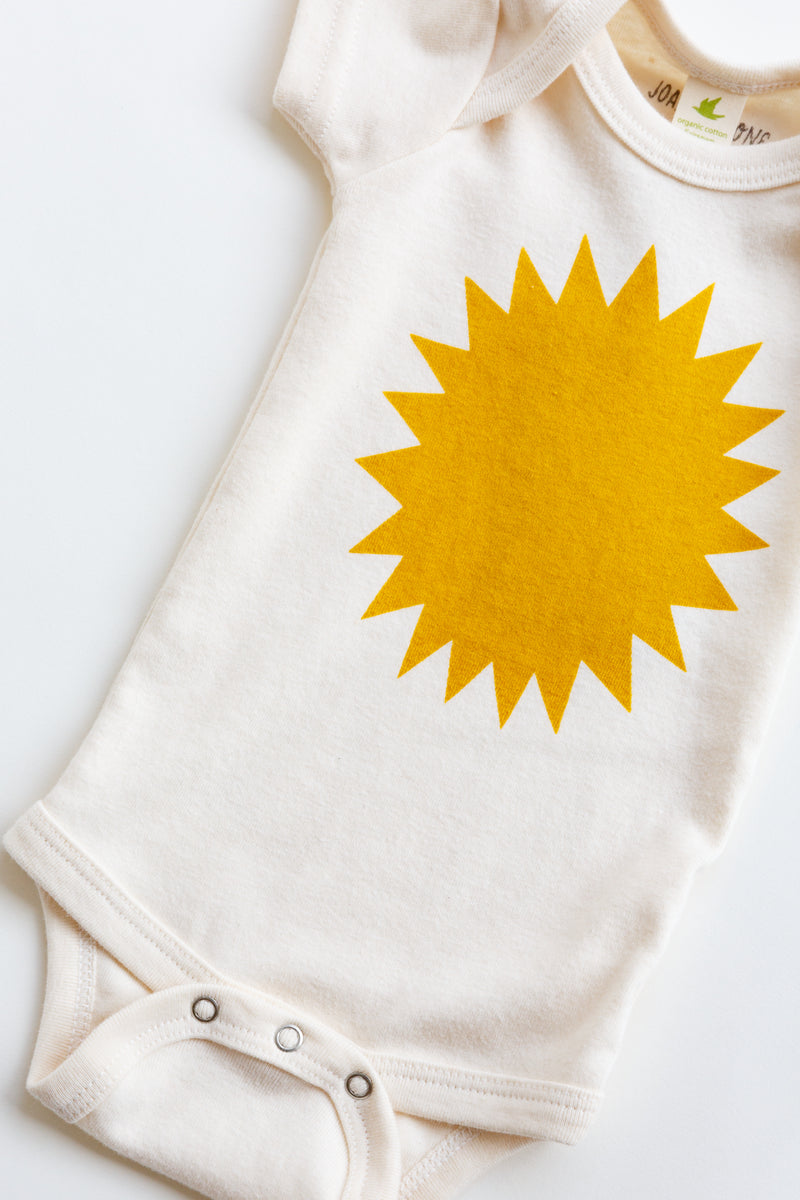 A Joan Ramone baby sunshine onesie printed on 100% organic cotton with non-toxic, water-based ink, laying flat on a table