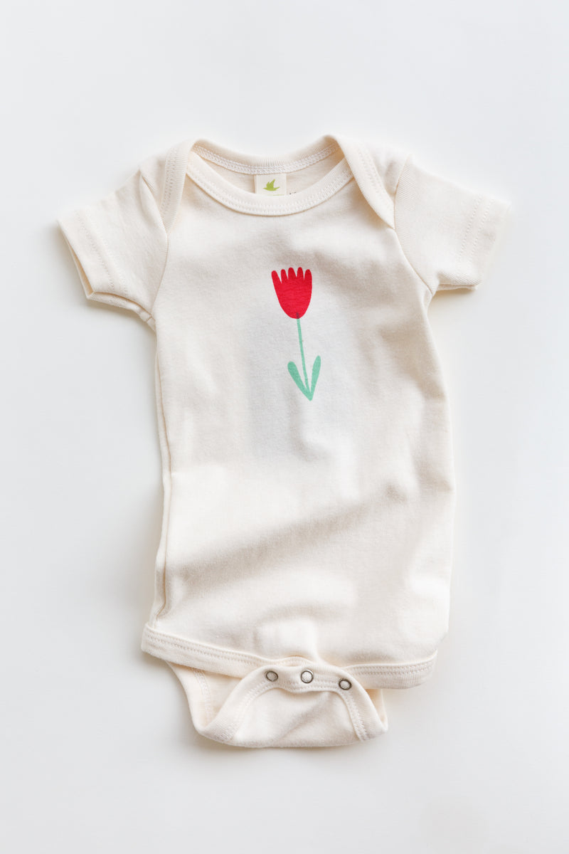 A Joan Ramone flower baby short-sleeved onesie, hand printed on 100% organic cotton with non-toxic, waterbased ink, laying on a flat table