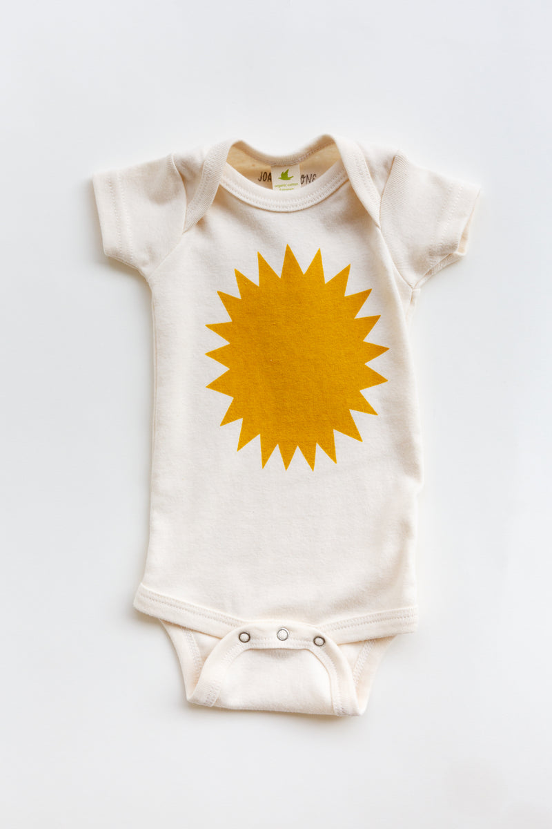 A Joan Ramone baby sunshine onesie printed on 100% organic cotton with non-toxic, water-based ink, laying flat on a table