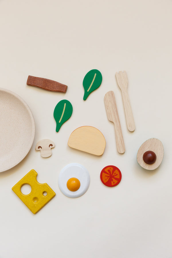 Children's breakfast toy set including a plate, silverware, slice of bread, half of an avocado, 2 leaves of baby spinach, a bacon strip, sunny-side-up egg, mushroom, slice of tomato, and slice of cheese