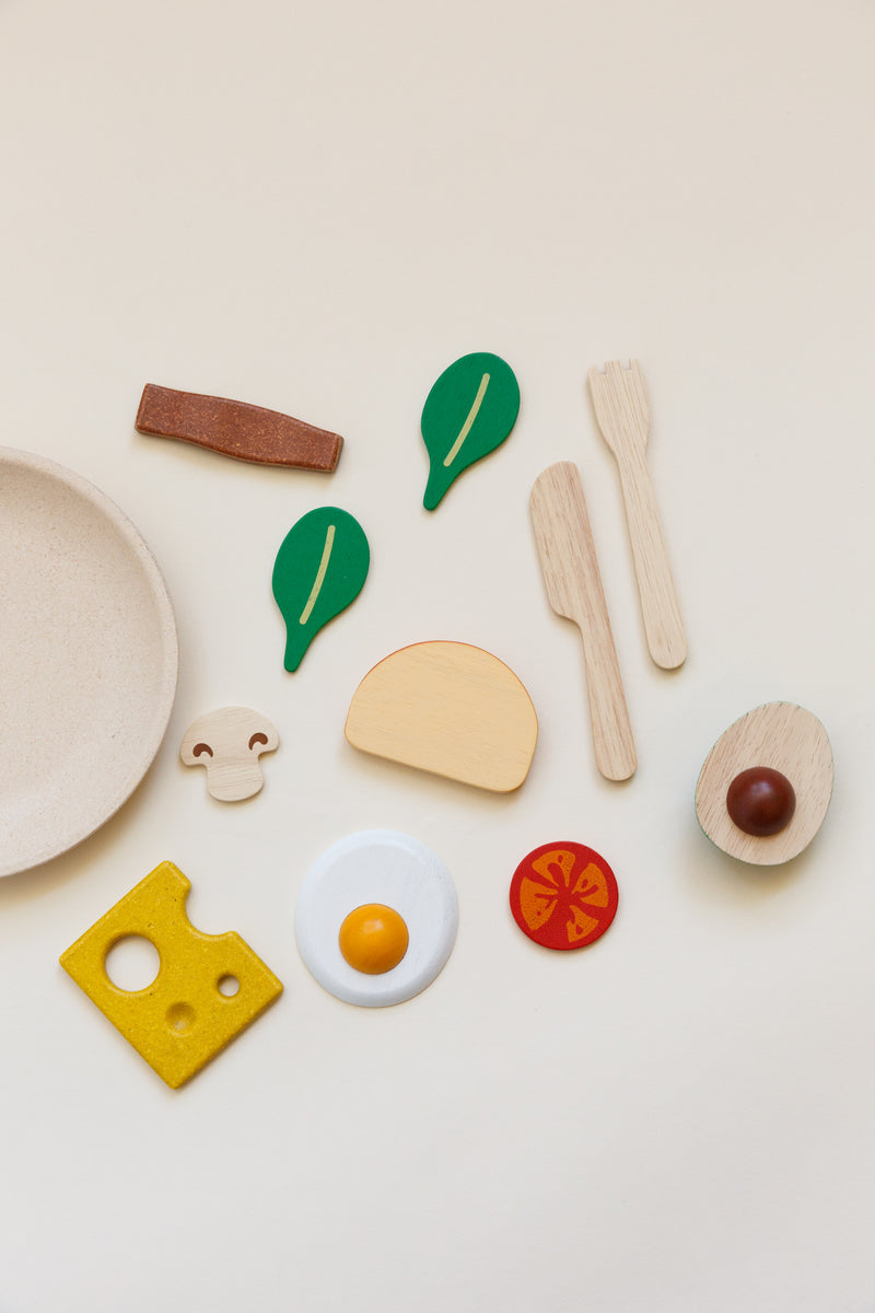 Children's breakfast toy set including a plate, silverware, slice of bread, half of an avocado, 2 leaves of baby spinach, a bacon strip, sunny-side-up egg, mushroom, slice of tomato, and slice of cheese