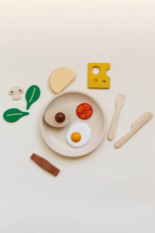 Children's breakfast toy set including a plate, silverware, slice of bread, half of an avocado, 2 leaves of baby spinach, a bacon strip, sunny-side-up egg, mushroom, slice of tomato, and slice of cheese