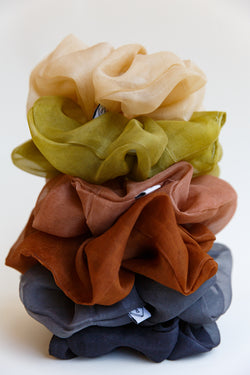 A stack of different colored Rosemarine scrunchies made with silk organza and dyed using plant matter and organic materials in Detroit