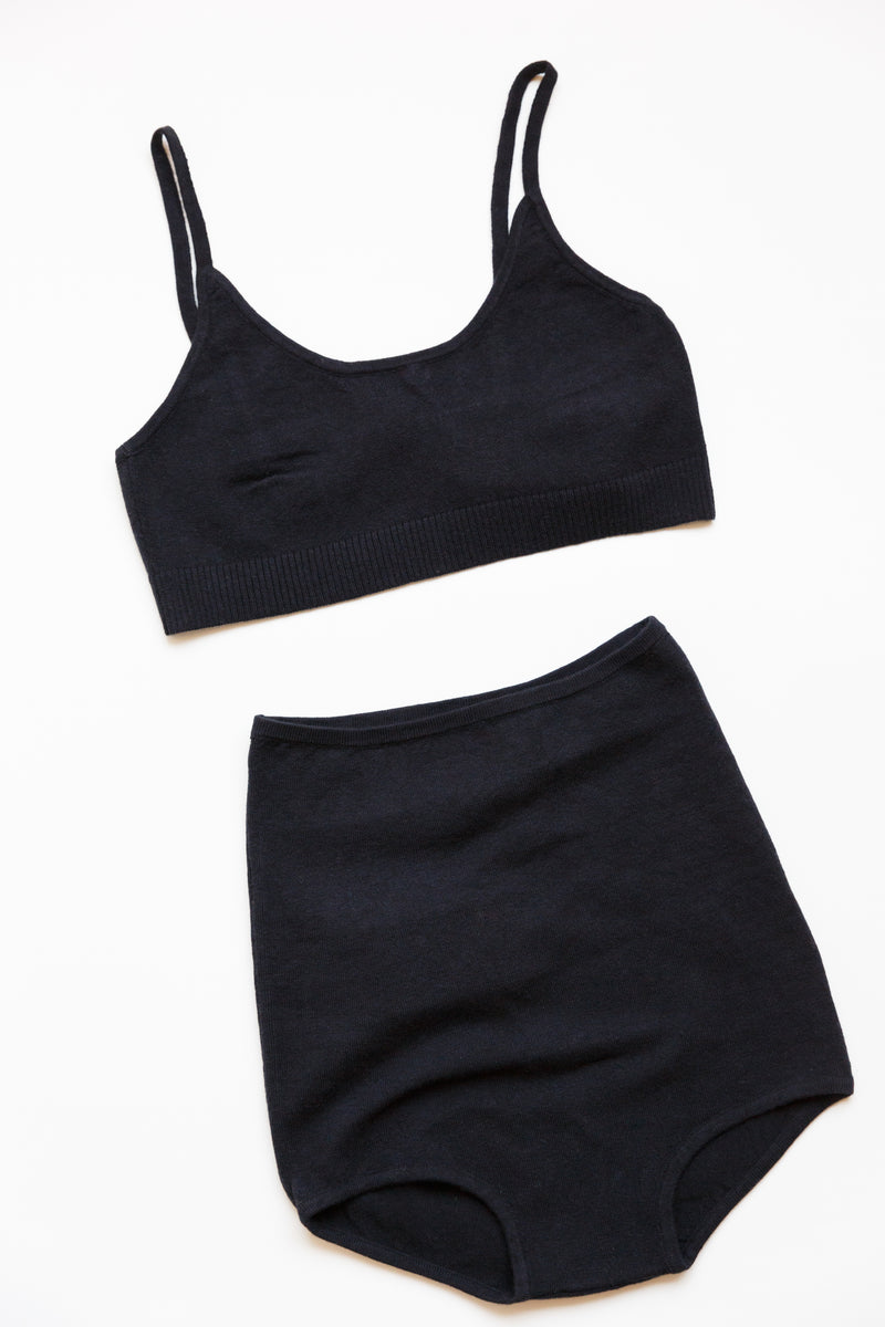 A black cotton silk sporty bralette with bottom ribbing on display on a table with a matching high-waisted panty