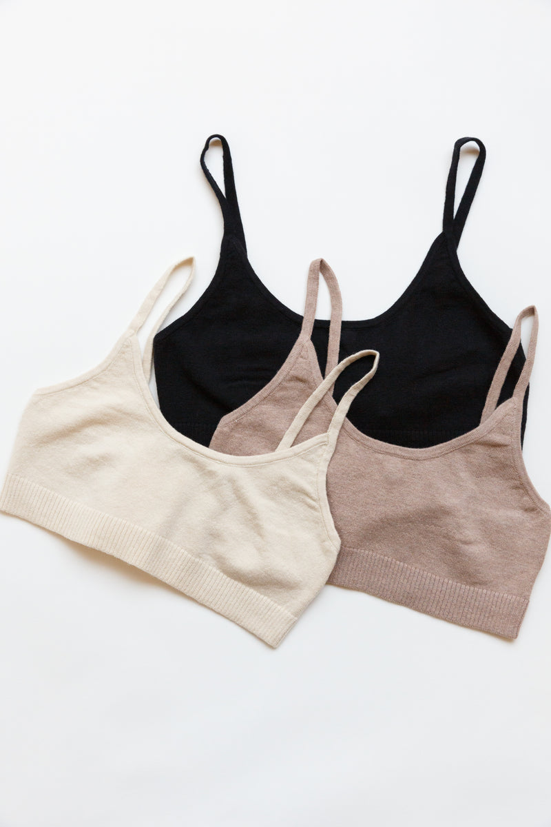 A collection of different colored cotton silk sporty bralettes with bottom ribbing laying on a flat table