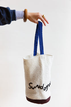 A person holding a hand-crocheted bucket bag with Sunday Morning embroidered letters