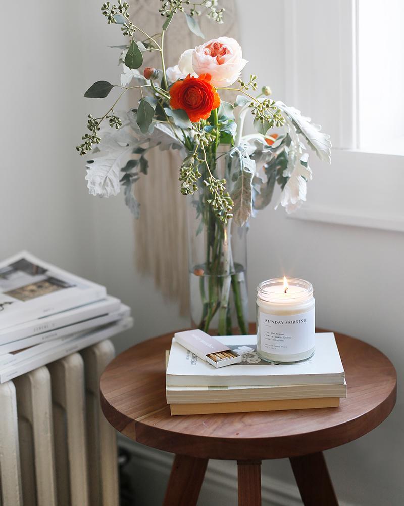 A Brooklyn Candle Studio jar in Sunday Morning scent on a table with flowers