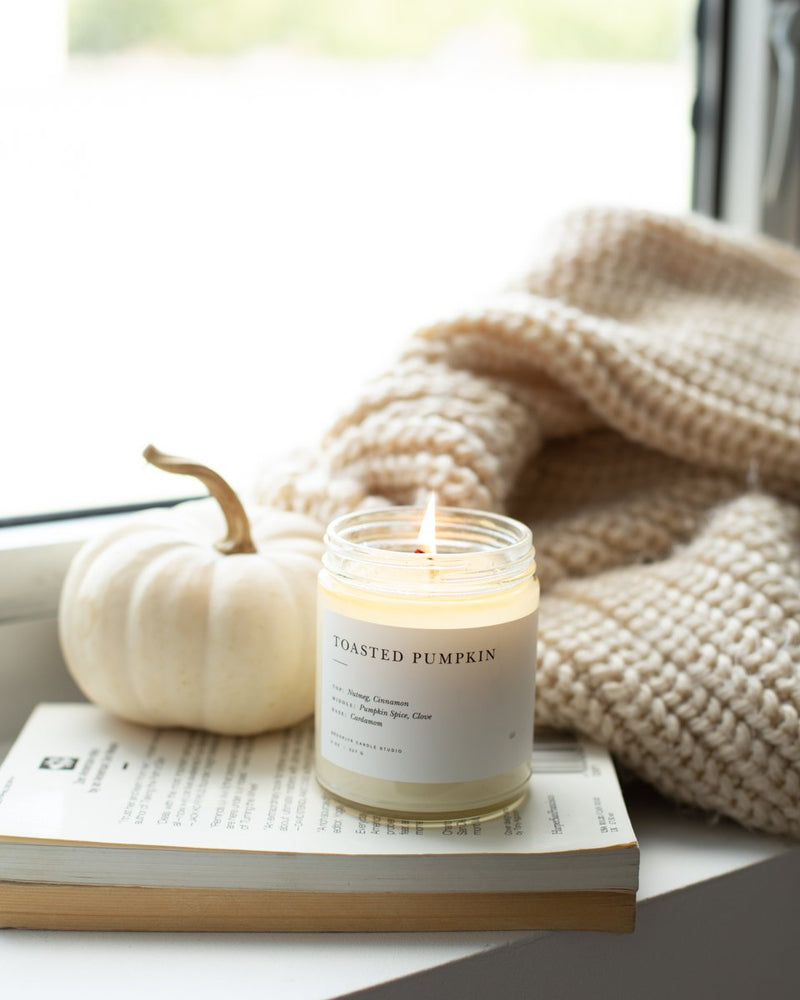 A Brooklyn Candle Studio jar in Toasted Pumpkin scent on a stack of books by a window