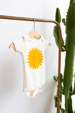 A Joan Ramone baby sunshine onesie printed on 100% organic cotton with non-toxic, water-based ink, on a hanger