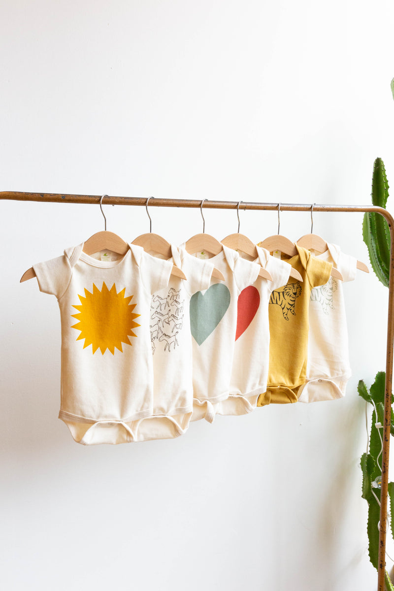 A Joan Ramone baby sunshine onesie printed on 100% organic cotton with non-toxic, water-based ink, on a hanger with other onesies
