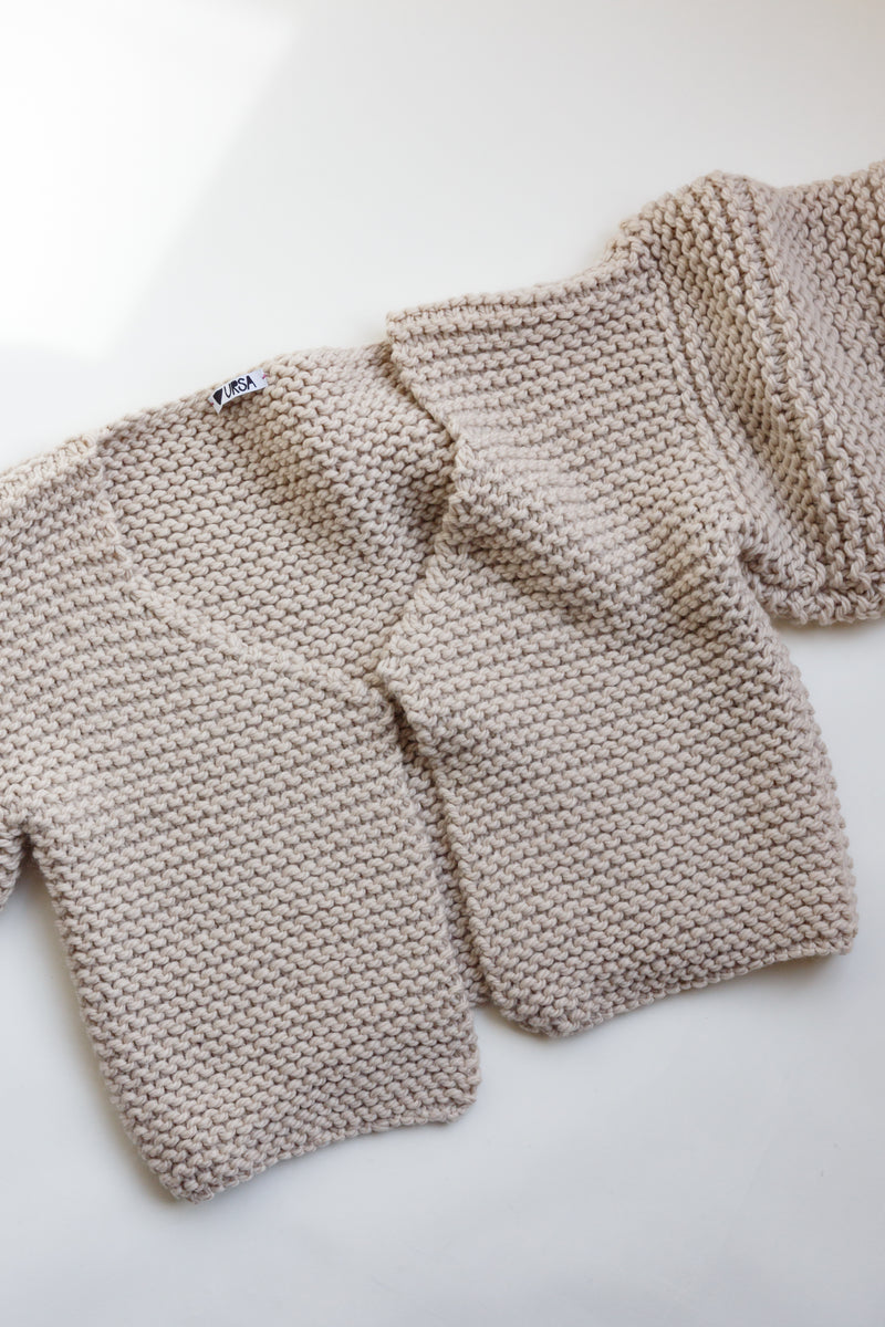 Handcrafted by women artisans in South America and made from the highest quality natural fibers sourced in Patagonia and The Andes, this chunky merino wool cardigan sweater is slightly cropped and is on display on a flat table