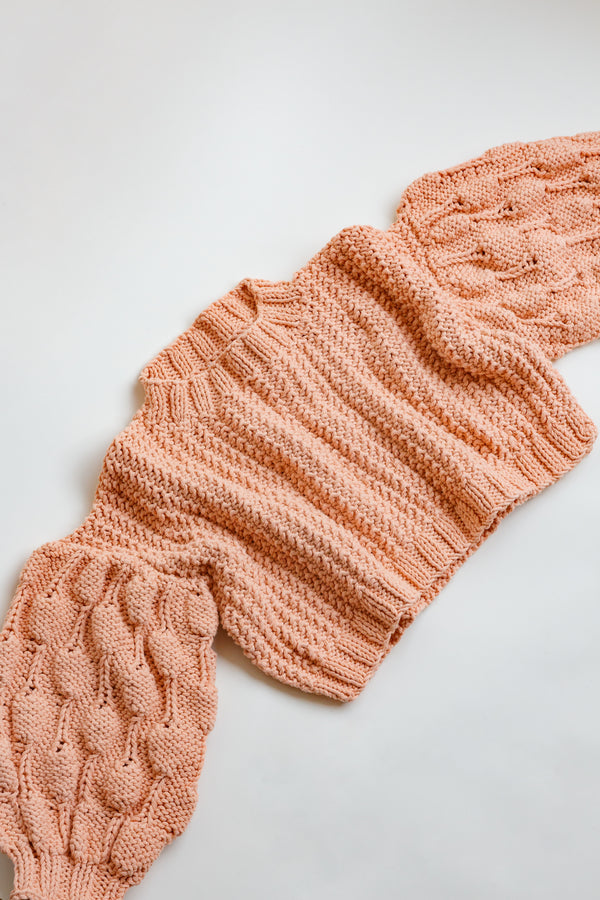 Handcrafted by women artisans in Argentina, this oversized chunky cotton pullover sweater features balloon sleeves from Ursa Textiles and is laying flat on display on a table
