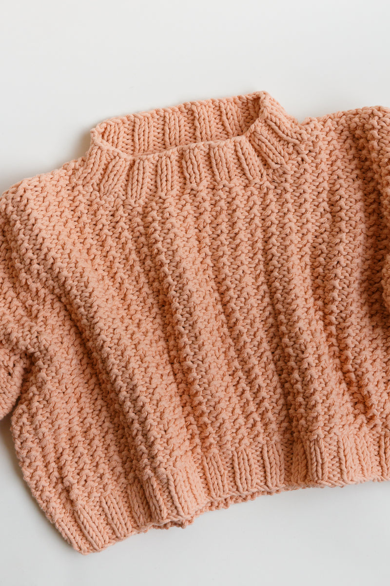 Handcrafted by women artisans in Argentina, this oversized chunky cotton pullover sweater features balloon sleeves from Ursa Textiles and is on display on a flat table