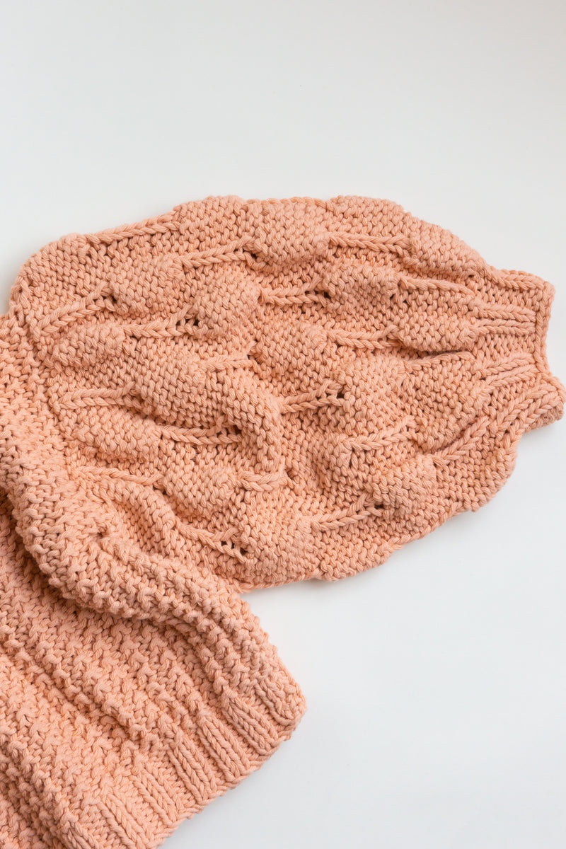 Handcrafted by women artisans in Argentina, this oversized chunky cotton pullover sweater features balloon sleeves from Ursa Textiles and is on display on a flat table