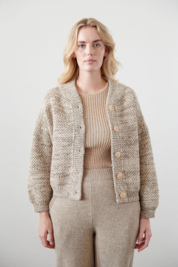 Model wearing a cropped wide cardigan featuring unvarnished wood buttons and a high, rounded collar made of wool/alpaca blend chain yarn
