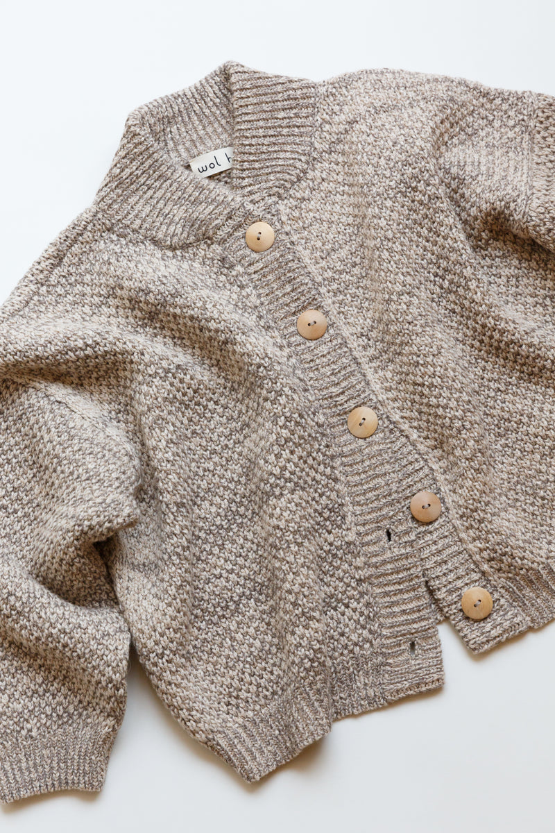 A cropped wide cardigan featuring unvarnished wood buttons and a high, rounded collar made of wool/alpaca blend chain yarn is on display on a flat table